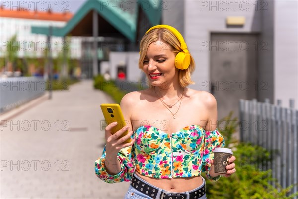 Pretty blonde woman listening to music in the city with yellow headphones and the phone