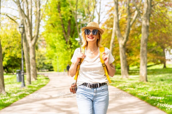 A blonde tourist woman smiling with a hat and sunglasses walking in the spring in a park in the city