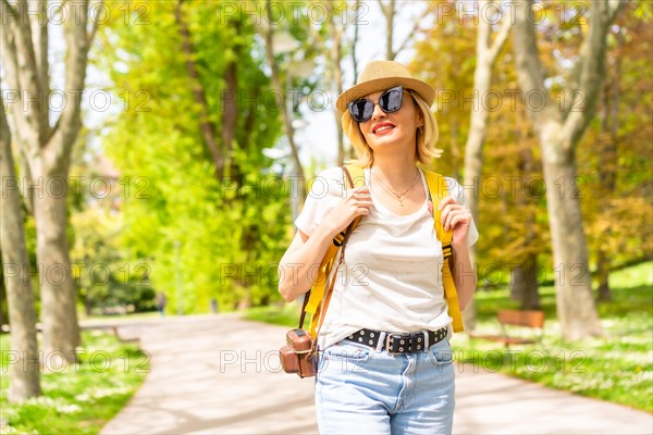 A tourist blonde woman in a hat and sunglasses visiting in the spring in a park in the city