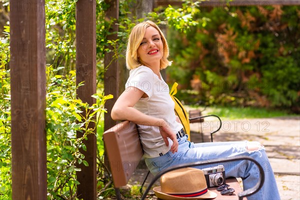 Portrait of a blonde tourist girl on summer vacation sitting on a bench in a park