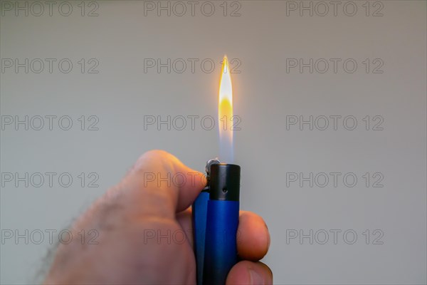 Mans hand lighting a blue lighter with copy space and light background