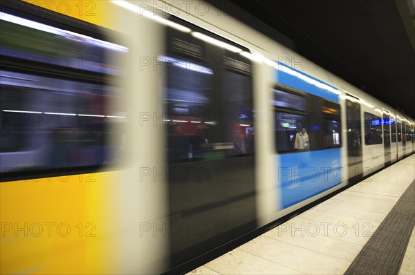 Travellers wearing Corona masks wait on the platform and are reflected in windows