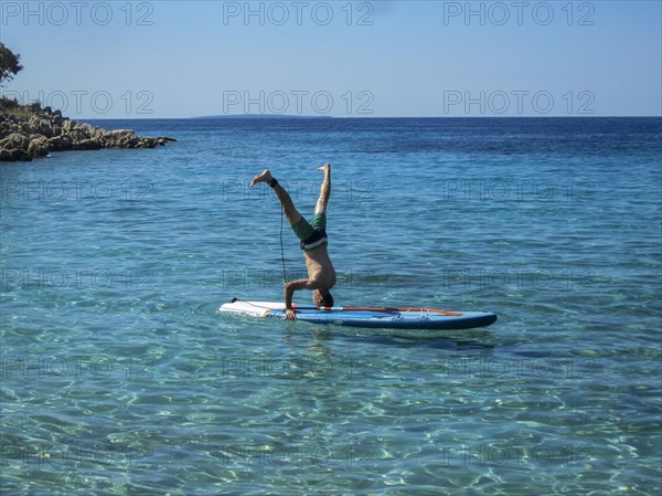 Man doing headstand on a SUP in crystal clear water