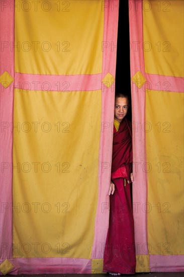 Young monk looking out from behind a curtain