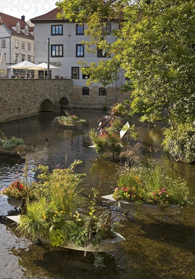 Zinc tubs in the shape of boats with flowering plants on the river Gera