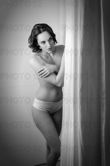 Woman dressed only in panties stands behind a curtain