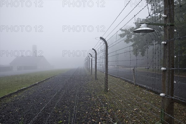 Reconstructed camp fence with crematorium in the fog at beech forest concentration camp