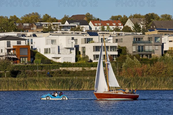 A sailboat and a pedal boat in front of the houses at the Phoenix See in Dortmund