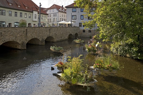 Zinc tubs in the shape of boats with flowering plants on the river Gera