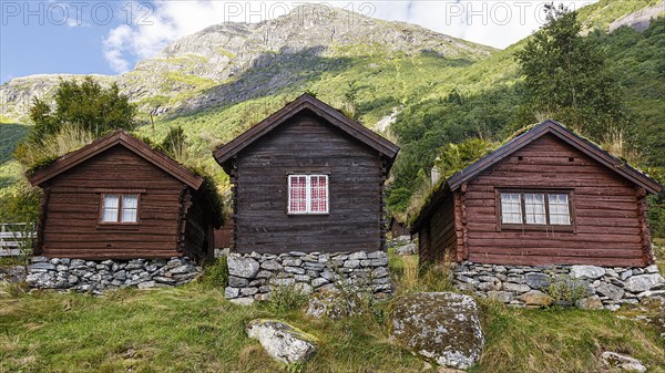 Three wooden huts stand on a mountain in Norway