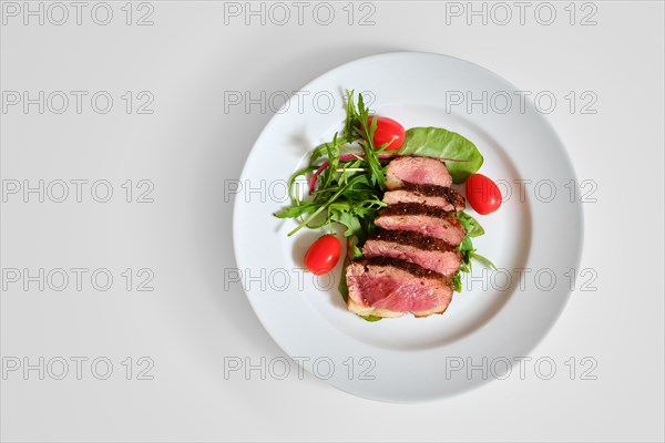 Top view of grilled duck breast medium rare served on a plate with arugula and corn salad