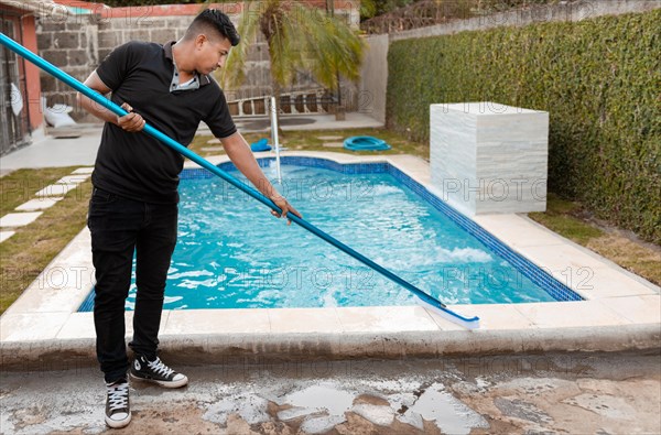 Swimming pool cleaning with brush. Maintenance person cleaning swimming pool with brush