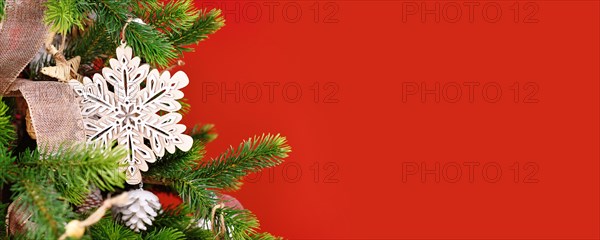 Christmas banner with tree branch with natural wooden snowflake ornament in front of red background with copy space