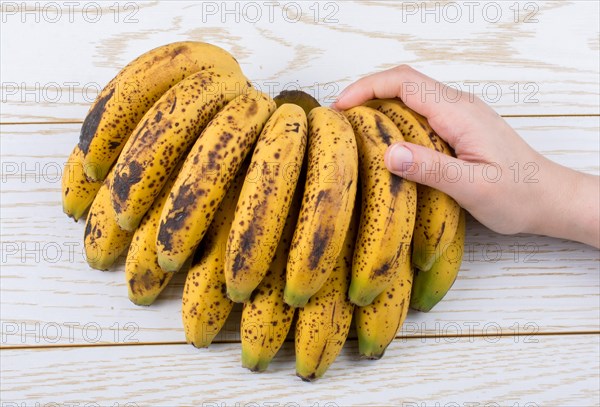 Hand holding bunch of freckled bananas on a wooden texture