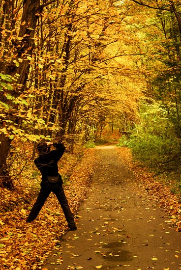 Photographer taking photo of autumn landscape of a road