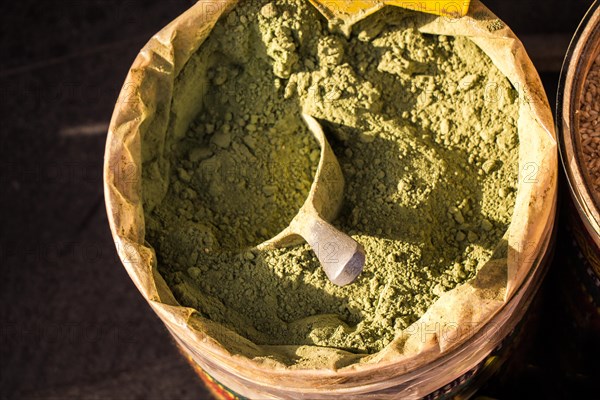 Dry henna in a bucket with a wooden shovel in it