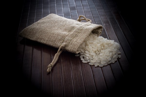 A straw pouch full of uncooked rice on a wooden background