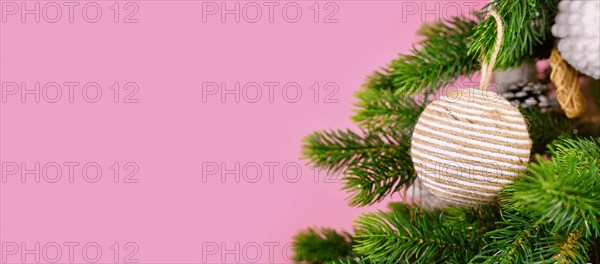 Banner with Christmas tree branches with natural ornament bauble made from beige jute rope on pink background
