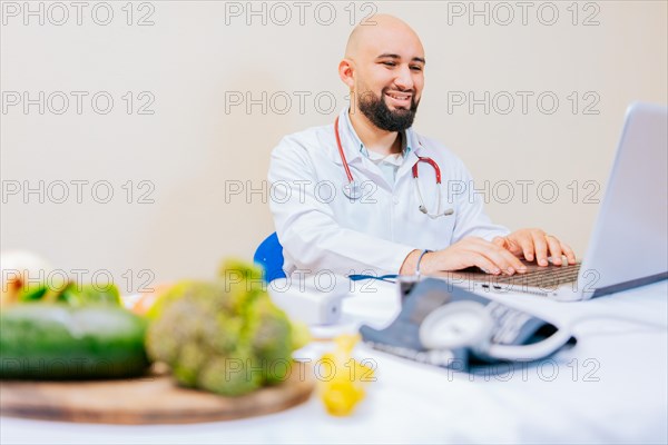 Smiling nutritionist with laptop at desk. Nutritionist doctor using laptop at workplace. Bearded nutritionist doctor working on laptop at desk