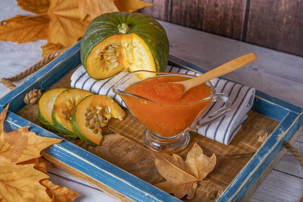 Homemade pumpkin marmalade in a glass jar on a wooden tray with dried leaves