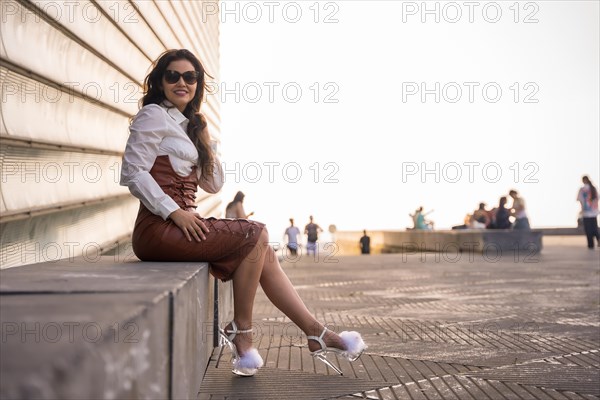 Portrait of a pretty brunette woman in a leather skirt sitting in a sunset wearing sunglasses