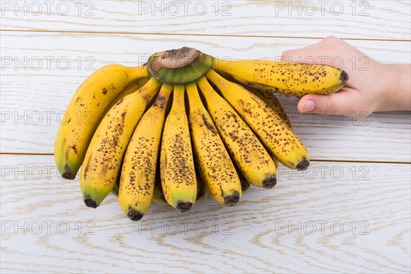 Hand holding bunch of freckled bananas on a wooden texture