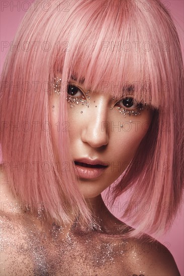 Beautiful woman in a pink wig and creative makeup with rhinestones. Beauty face. Photo taken in the studio