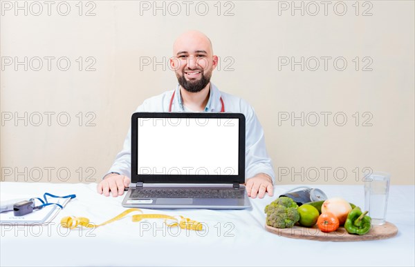 Nutritionist man showing laptop screen. Nutritionist at desk showing blank screen of laptop. Smiling nutritionist showing an advertisement on the laptop