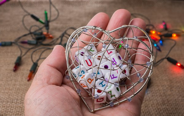 Hand holding a heart cage full of alphabet dice on a Christmas light textured background