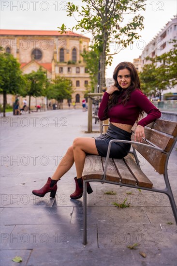 A brunette woman in a leather skirt sitting in the city