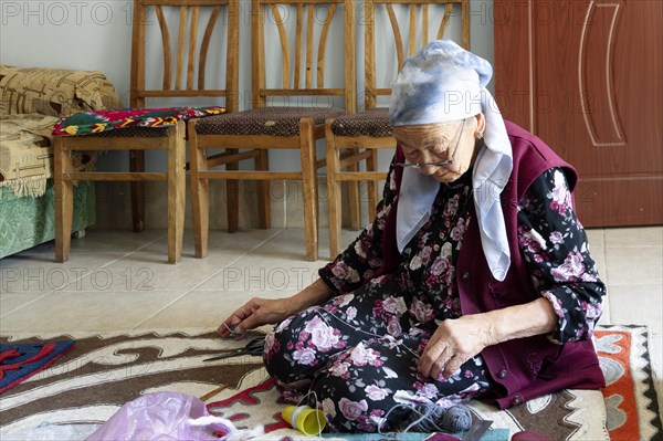 Old woman sitting on the floor and sewing carpet in an artisanal factory