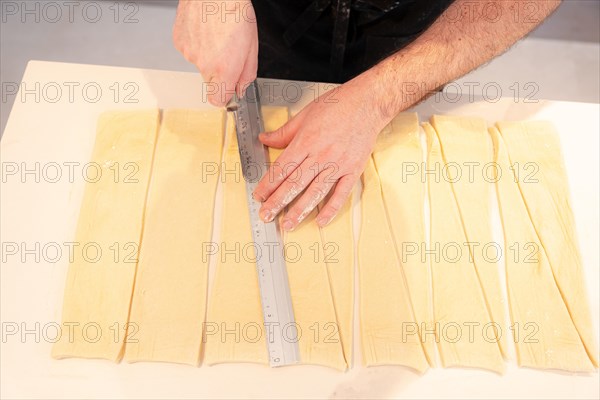 Detail of the hands of a man baking croissants making triangular cuts in the puff pastry