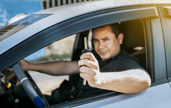 Driver in his car showing the keys out the window. Happy man showing his new car keys