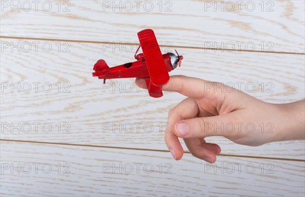 Hand holding a red toy plane on a on wooden texture