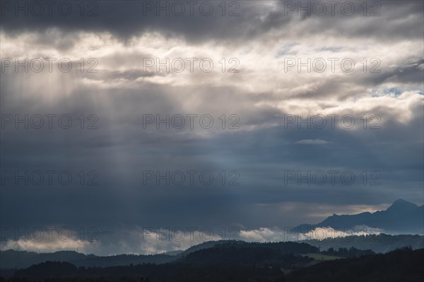 Rays of sunshine fall through impressive cloudy skies onto the mountain landscape around Murnau
