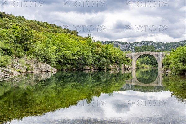Old bridge Pont dIssensac on the French river Herault on a cloudy day
