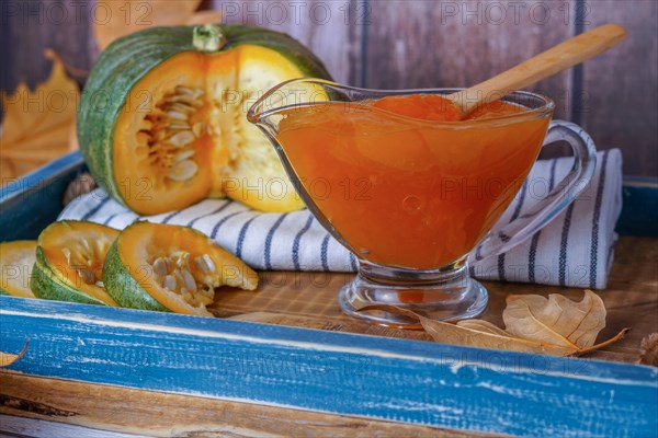 Homemade pumpkin marmalade in a glass jar on a wooden tray with dried leaves