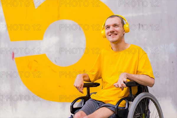 Portrait of a disabled person dressed in yellow in a wheelchair smiling listening to music