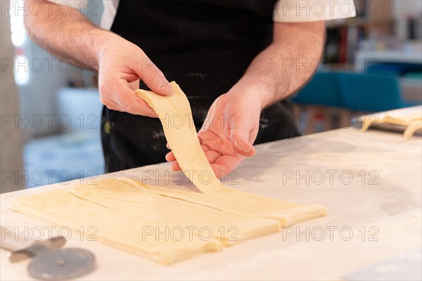 Detail of the hands of a man baking croissants collecting the triangular cuts of the puff pastry