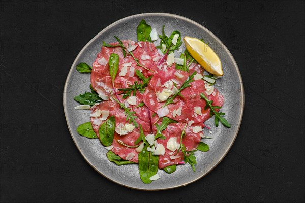 Top view of marbled beef carpaccio with arugula and chard leaves