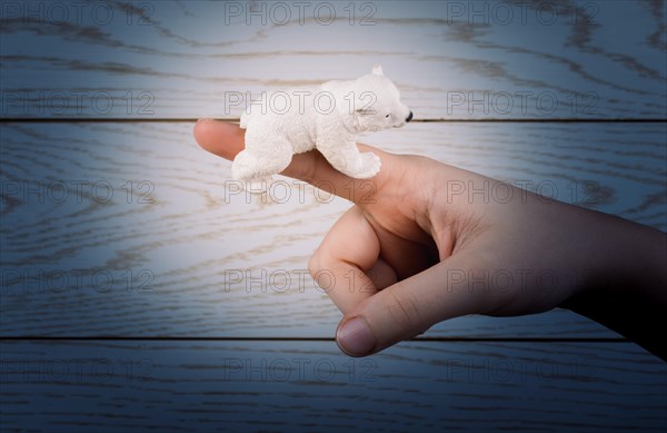 Hand holding a Polar bear model on a wooden background