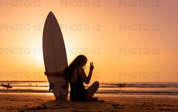 Silhouette of a surfer woman on a beach at sunset making the victory sign