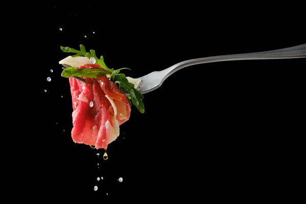 Sprinkling piece of marbled beef carpaccio on fork with lemon juice over black background