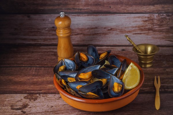 Steamed mussels with lemon in clay pot with metal mortar and pepper shaker