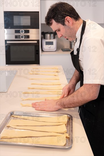 A man baking croissants picking up the triangular cuts from the puff pastry