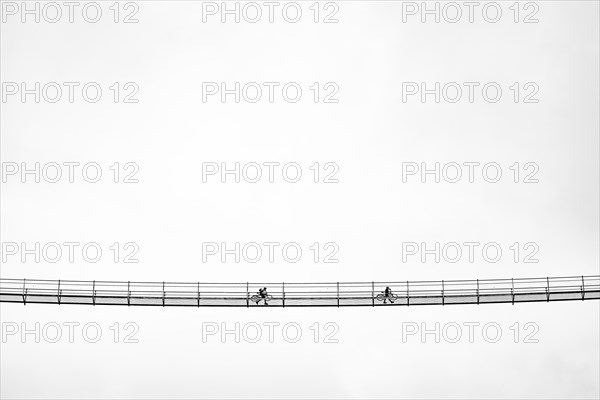 Suspension bridge with two cyclists against a white sky