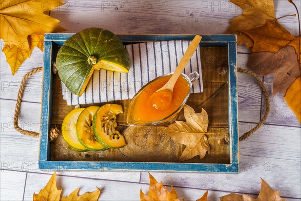 Top view of homemade pumpkin marmalade in a glass jar on a wooden tray with dried leaves
