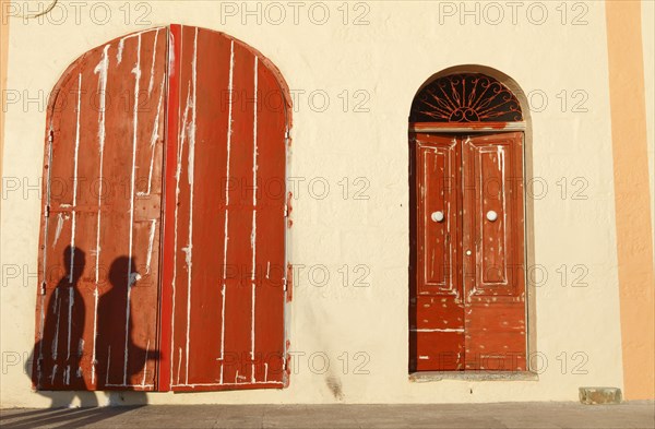 People casting shadows on red doors