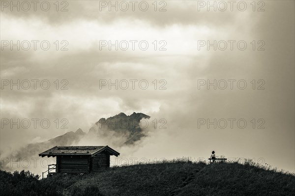 Mountain hut with bench and climber and dramatic clouds in the background