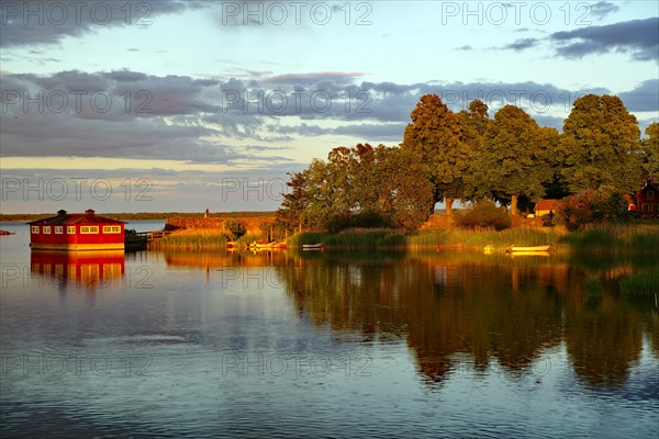 Trees and a small red wooden house reflected in the calm water